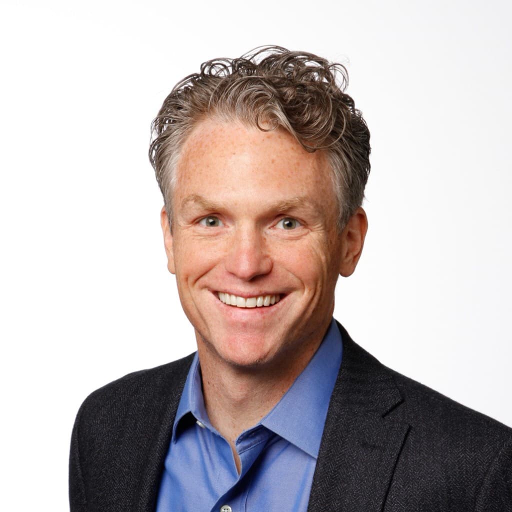 Professional headshot of Nathan Spear, salt-and-pepper hair, light blue shirt and dark blazer, on a clean white background.